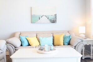 A living room with a beige sofa, a white coffee table, and a painting of a pier.