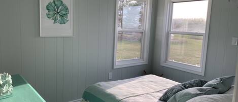 A bedroom with a bed, two windows, a wall-mounted picture, and a green dresser.