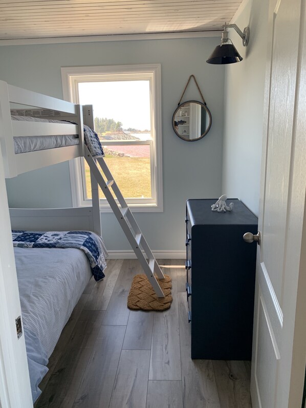 A room with a bunk bed, a desk, a mirror, and a window with a view of the outdoors.