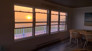 A room with a large window overlooking a balcony with a view of the sunset over the water. - Oceanfront beach cottage panoramic views spectacular sunsets sandbars warm water (Pictou)