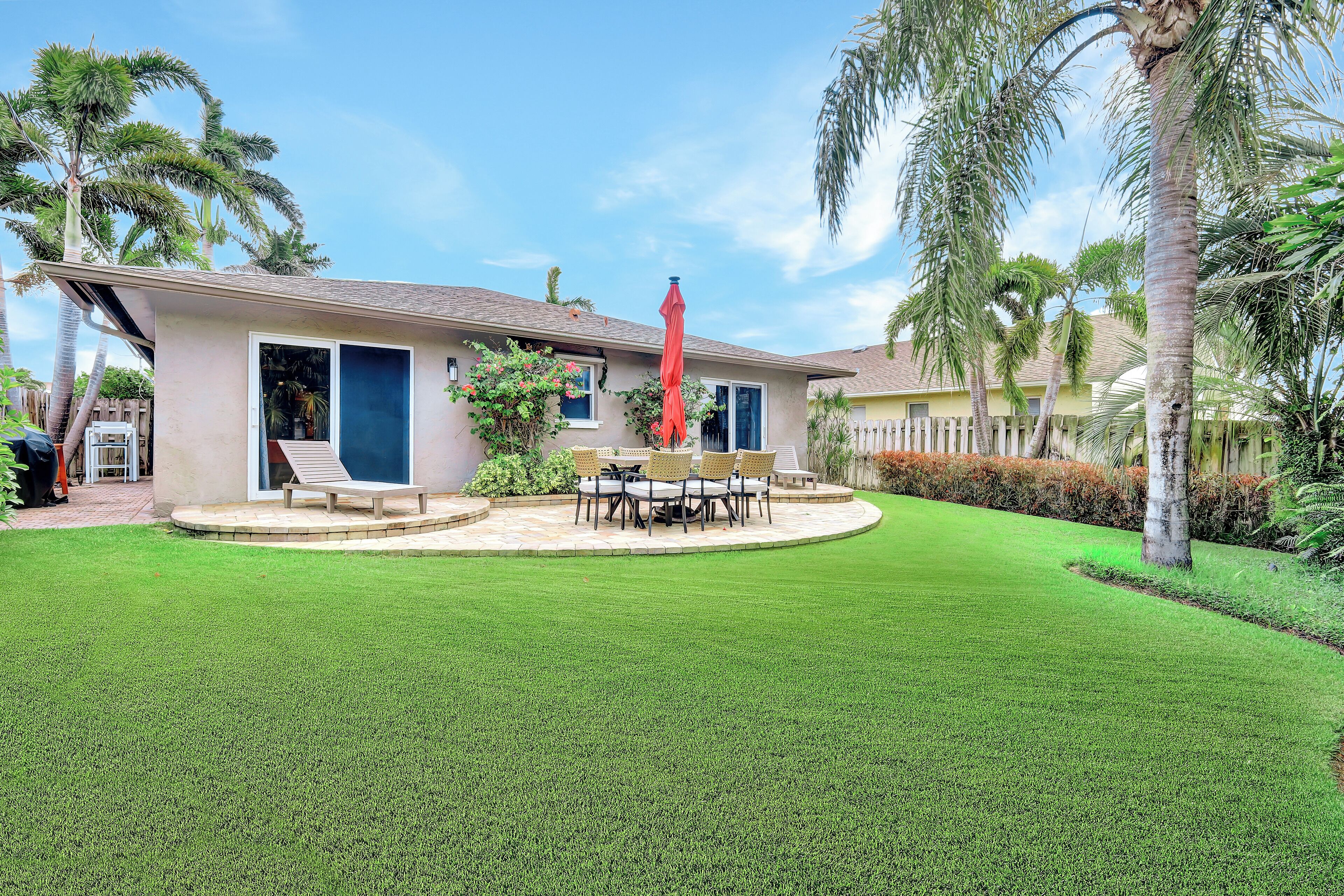 A house with a well-maintained lawn, a patio with outdoor furniture, and a red umbrella.