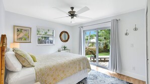 A bedroom with a bed, a ceiling fan, a window with curtains, a framed picture, and a view of the outdoors.