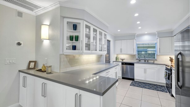 A modern kitchen with white cabinetry, a central island, stainless steel appliances, and a built-in cabinet with glass doors.