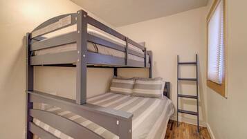 A bunk bed room with a ladder, wooden flooring, and a window with blinds.