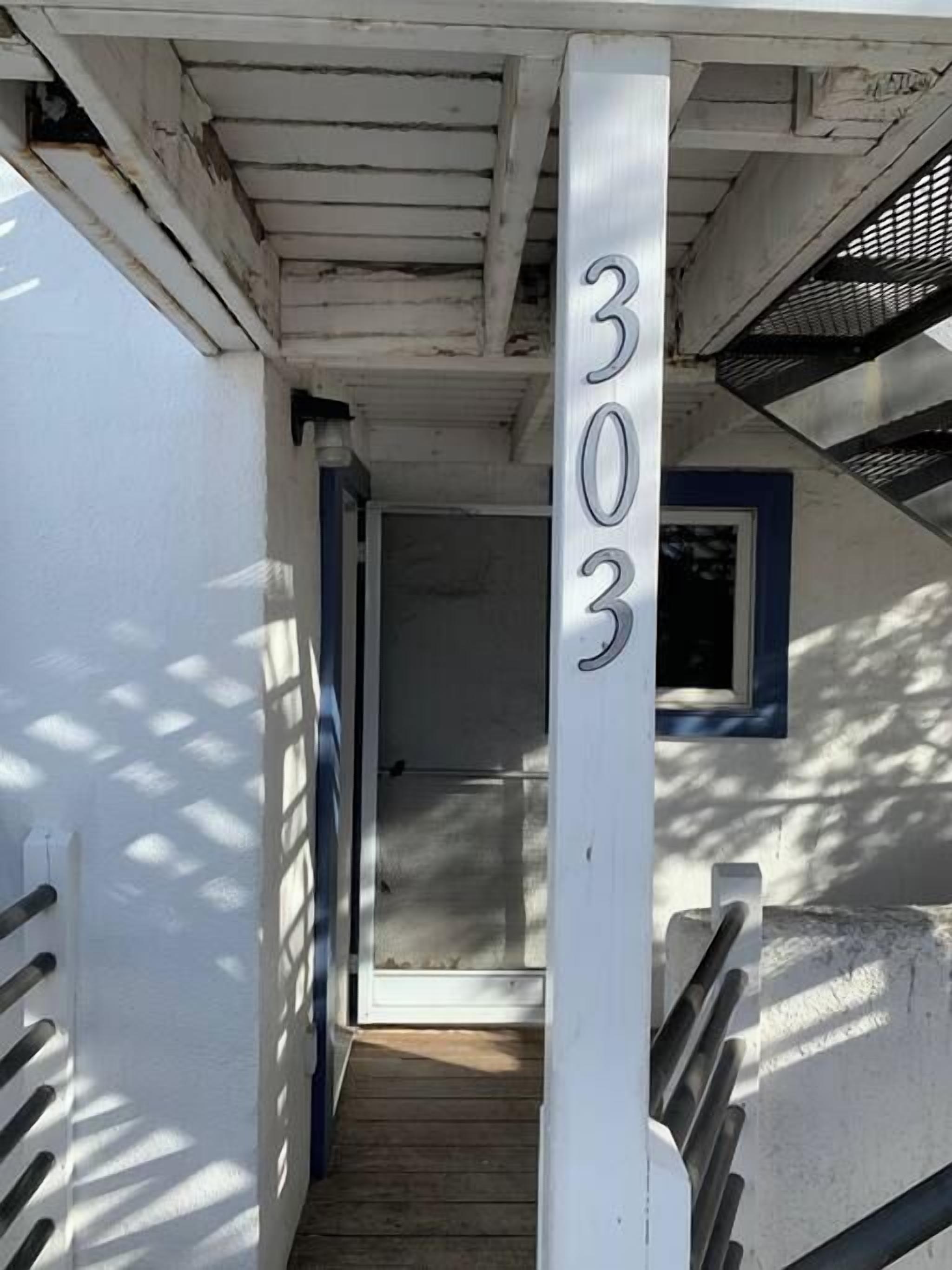A staircase leading to a door with the number 303 on it, a wooden floor, and a white wall with a window.