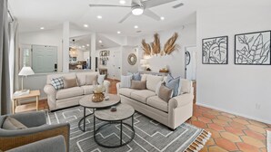 A spacious living room with a beige sofa set, a round coffee table, and a ceiling fan. - Charming Retreat | Pool, Walk to Park & Coffee (Jacksonville Beach)