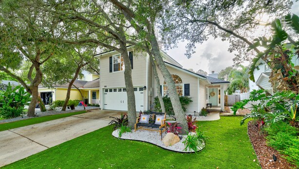 A two-story house with a well-maintained lawn, a bench, and a variety of plants. - Charming Retreat | Pool, Walk to Park & Coffee (Jacksonville Beach)
