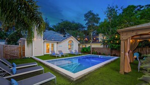 A backyard with a swimming pool, lounge chairs, and a wooden pergola. - Charming Retreat | Pool, Walk to Park & Coffee (Jacksonville Beach)