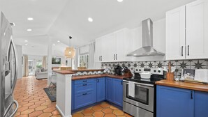 A modern kitchen with white and blue cabinets, a stainless steel range hood, and a tiled backsplash. - Charming Retreat | Pool, Walk to Park & Coffee (Jacksonville Beach)