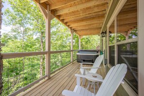 Een overdekt terras buiten met houten vloer, witte Adirondack-stoelen en een barbecueplek.