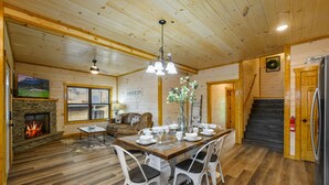 Interior acogedor de una cabaña con comedor, chimenea y una escalera que lleva a otro nivel.