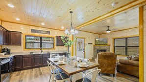 Interior de una cabaña de madera con una mesa de comedor preparada para cuatro personas, una chimenea y una zona de estar acogedora.