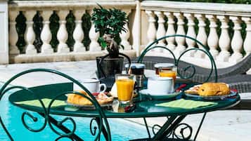 Une table à manger avec des aliments pour le petit-déjeuner, une plante en pot et une vue sur une piscine et un jardin.