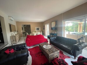 Een woonkamer met een rode bank, zwarte leren fauteuils, een houten salontafel en een hond op een lederen divan.