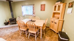 Uma sala de jantar com mesa e cadeiras de madeira, fogão embutido e armário com prateleiras.