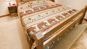 Quarto com cama de madeira, duas mesas de cabeceira com abajures, janela com cortinas e luminária no teto.