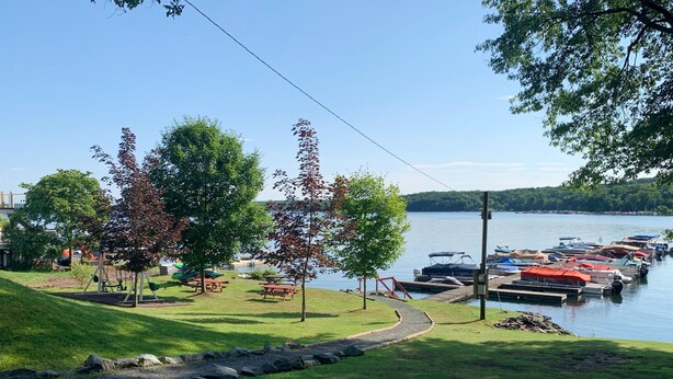 Un parque junto al lago con mesas de picnic, columpios y un muelle con barcos.