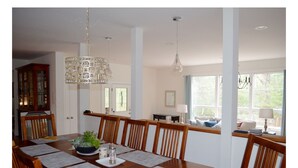 Un comedor con una mesa de madera dispuesta para cuatro personas, rodeada de sillas. Encima de la mesa, un candelabro, y a la derecha, una ventana con cortinas.