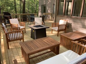 An outdoor deck with wooden furniture, including chairs and tables, and a built-in fire pit.