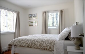 A bedroom with a bed, a bedside lamp, and two windows with curtains.