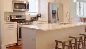 Una cocina moderna con armarios blancos, electrodomésticos de acero inoxidable y una isla central con taburetes de bar.