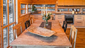 Een houten chalet van binnen met een eettafel, stoelen, een keukenhoek en grote ramen.