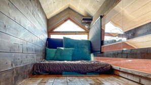 Een knus loft slaapkamer met schuine wanden, houten muren en een bed met blauw hoofdeinde.