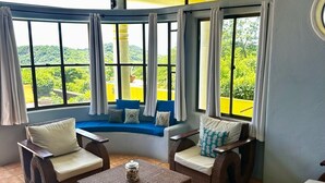 Ein Zimmer mit Korbmöbeln, Blick auf Grünflächen und einer gelben Wand.