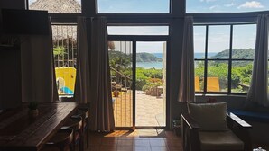 Ein geräumiges Zimmer mit einer großen Schiebetür zu einem Außenbereich mit Blick auf das Meer und die Hügel.