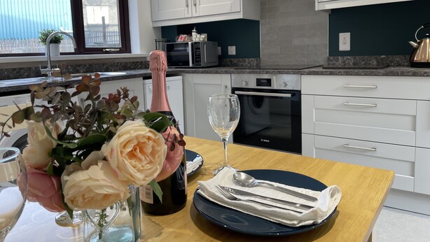 Een moderne keuken met witte kasten, een Bosch oven en een eethoek met een tafel voor twee personen.