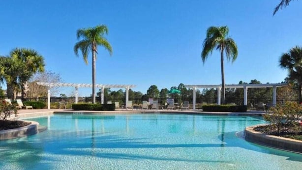 Ein klares Schwimmbecken mit einer Pergola, Palmen und einer gepflegten Umgebung.