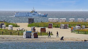 A beach with portable cabins, a ferry in the background, and a person walking. - Pet friendly home in Büsum with sauna (Büsum)