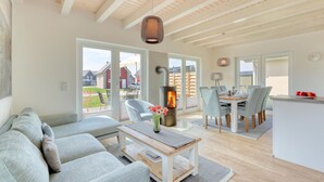 A spacious living room with a sofa, a coffee table, and a dining area with chairs and a table. A wood-burning stove is visible in the background. - Pet friendly home in Büsum with sauna (Büsum)