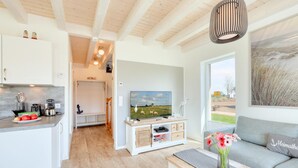 A modern kitchen with white cabinets, a dining area with a grey sofa, and a TV on a wooden stand. - Pet friendly home in Büsum with sauna (Büsum)