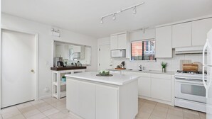 A modern kitchen with white cabinetry, a central island, a microwave, a stove, and a window with blinds. - Family vacation home at Cultus Lake - Pet Friendly (Cultus Lake)