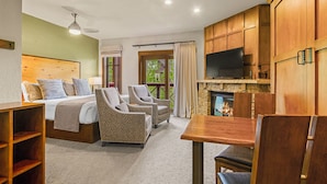 Une chambre d’hôtel avec un lit, deux fauteuils, une table en bois, une télévision et une cheminée.