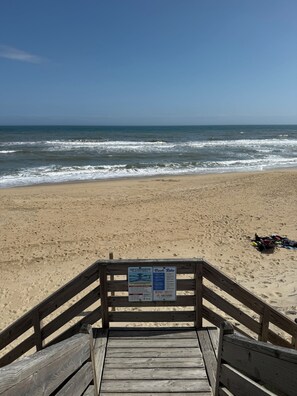 A wooden boardwalk leading to a sandy beach with a signboard displaying beach rules. - Serenity4Shore (Duck)