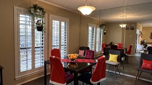 A dining area with a table set for four, surrounded by chairs with red accents, large windows with blinds, and a chandelier. - Momo's cozy  home 2BR/2BA with pool (Dallas)