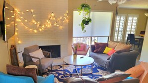 A living room with a fireplace, a ceiling fan, and a dining area in the background. - Momo's cozy  home 2BR/2BA with pool (Dallas)