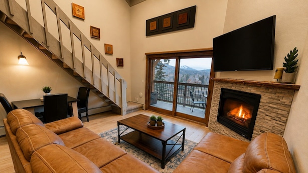 Un salón con chimenea, sofá de cuero, una mesa de centro, televisor y una escalera.