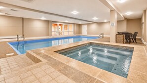 Una piscina con un área separada para hidromasaje, una puerta que da a otra habitación y una mesa con sillas.