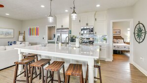 Un'ampia cucina con mobili bianchi, una grande isola con sgabelli, elettrodomestici in acciaio inossidabile e illuminazione a sospensione.