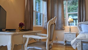 A room with a wooden desk, a white chair, a bed, and two windows with curtains. - Hale Hilo Bay Tropical Hideaway (Hilo)
