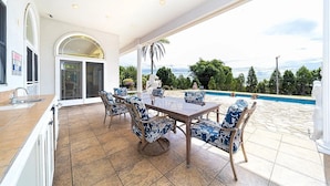 A spacious patio with a dining table and chairs, a pool, and a view of the ocean. - Hale Hilo Bay Tropical Hideaway (Hilo)