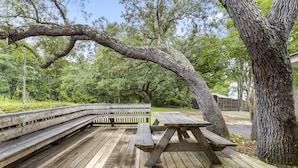 A wooden picnic table and benches on a deck surrounded by trees.