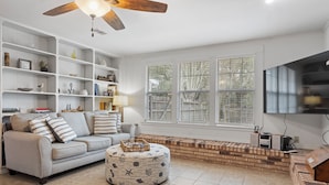 A living room with a sofa, ottoman, and shelves filled with books and decorative items.