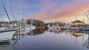 A marina with boats docked, a building with a dark roof, and trees in the background.