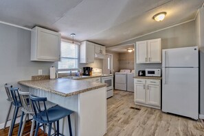 A kitchen with white cabinets, a granite countertop, a built-in microwave, and a refrigerator. - Manufactured Home Close to the Beach (Carolina Beach)