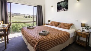 A hotel room with a large bed, a dining table, and a view of a field. - Lodge by the River - Studio 2 (Merrijig)