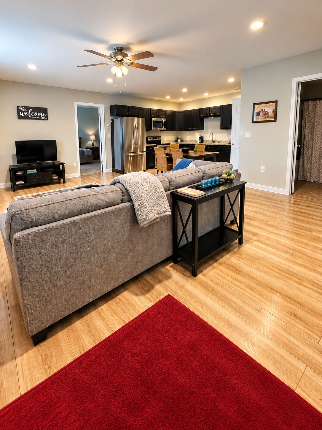 A modern living room with a sectional sofa, a red rug, a TV stand, and a ceiling fan.